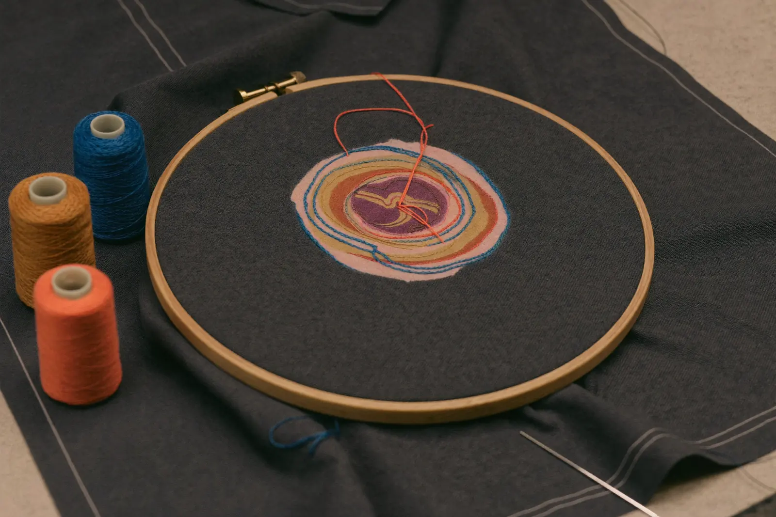 Grafikdesign Salzburg: Logo, Drucksorten und Preise im Überblick 2026 4 Grafikdesign Salzburg für Textilveredelung: Stickrahmen mit buntem Garn auf dunklem Stoff